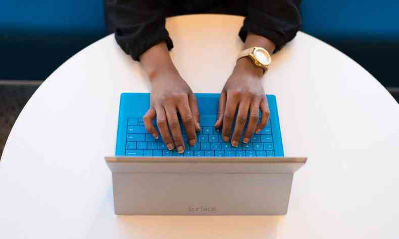 Fito tirada de cima mostra as mos de uma pessoa negra digitando em um laptop 