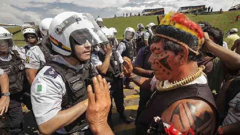 Fotografia colorida mostra grupo de indgenas em frente a policiais paramentados