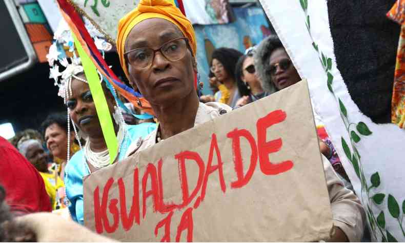Cartaz escrito 'igualdade j', segurado por uma mulher negra