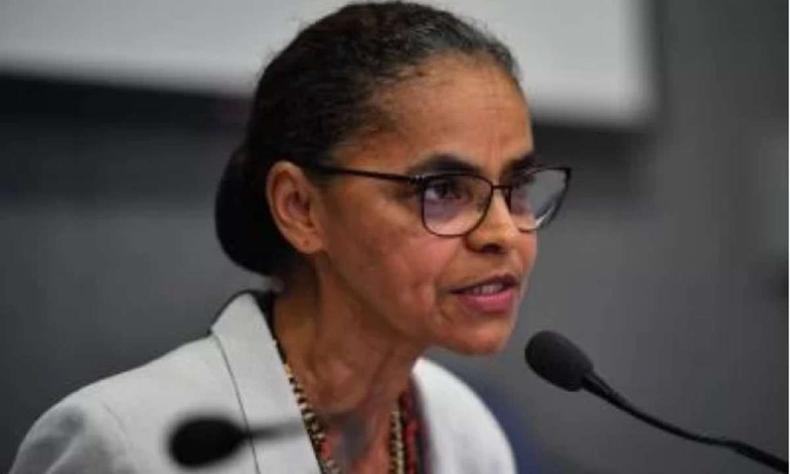 Marina Silva, de cabelos presos, culos e terno branco, fala ao microfone