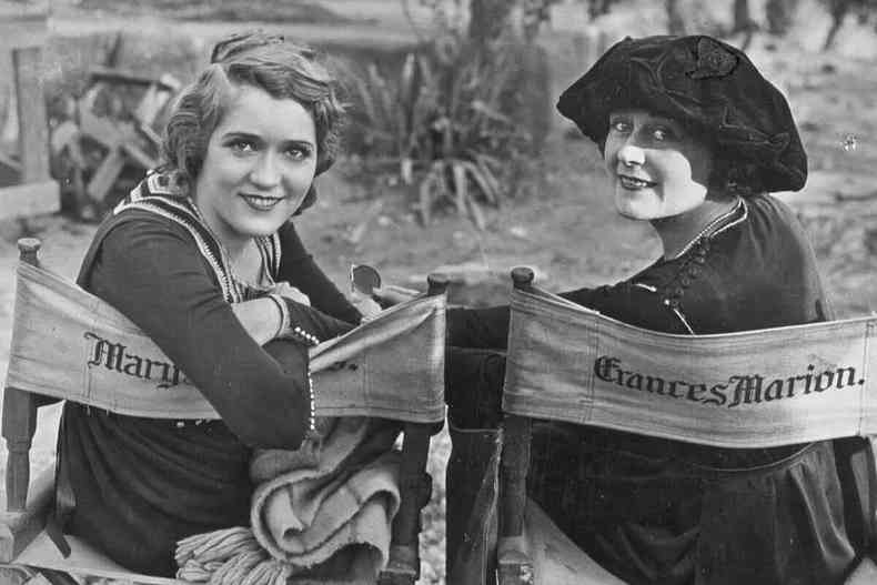 Atriz Mary Pickford e roteirista Frances Marion esto em set de filmangens sentadas em cadeiras onde esto escritos os nomes delas