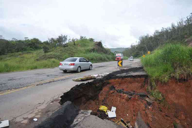 Estrada com cratera em uma das vias e um carro passando