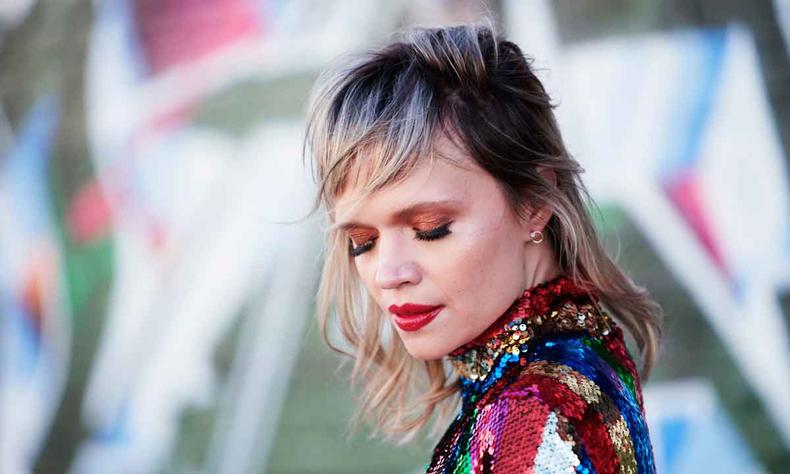 Maquiada e com blusa multicolorida, Alexia Bomtempo fecha os olhos e curva a cabea 