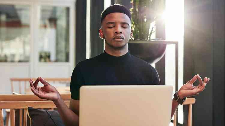 Homem meditando de olhos fechados em frente a laptop