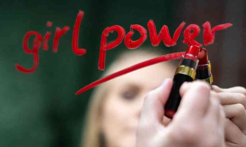 Mulher escrevendo 'girl power' com batom vermelho em um espelho
