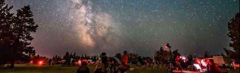 A group of people stargazing, the sky is lit with meteorites and the milky way