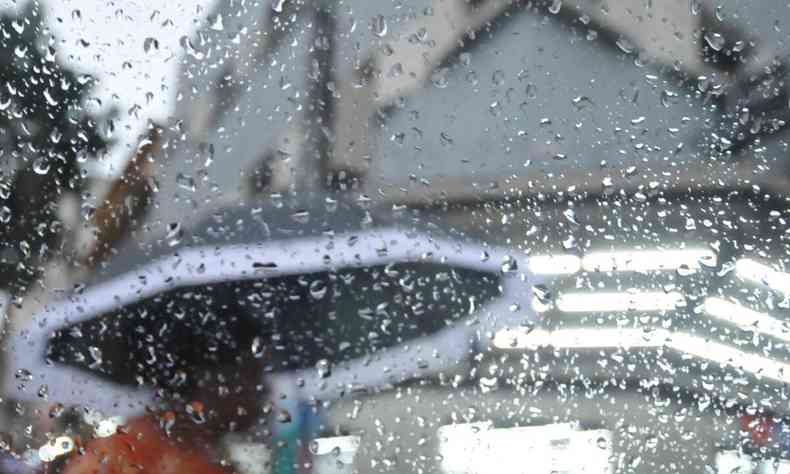 Imagem de uma pessoa com um guarda-chuva e o vidro molhado com gotas
