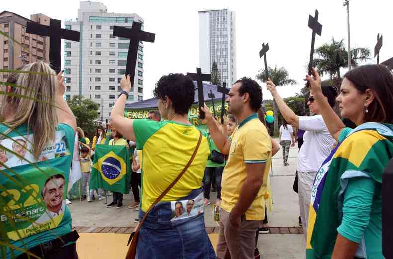 Apoiadores de Bolsonaro, de verde e amarelo, com cruzes pretas levantadas para cima
