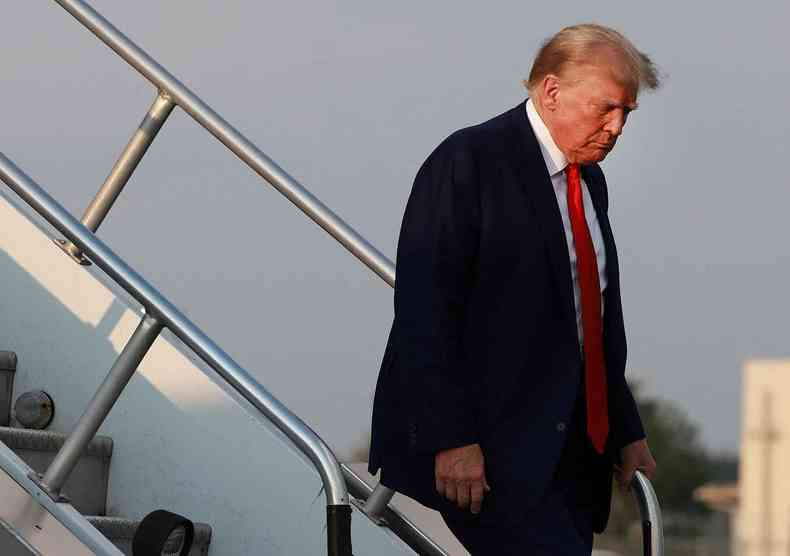 Trump descendo das escadas de um avio com a cabea baixa