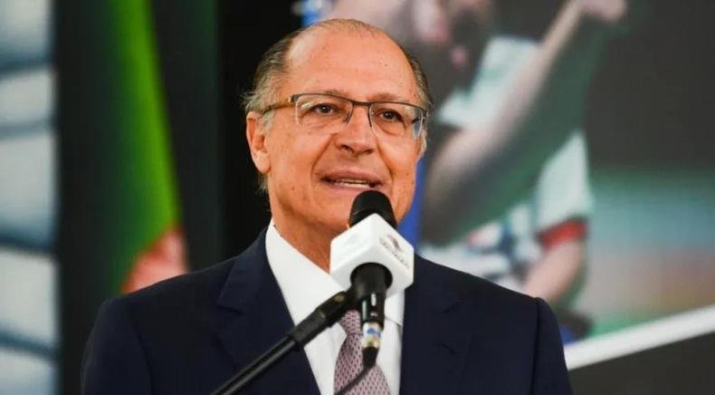 Geraldo Alckmin de terno preto falando em frente a um microfone