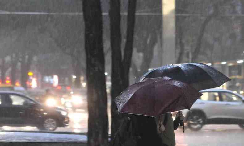 Imagem de pessoas andando sob a chuva com sombrinhas 