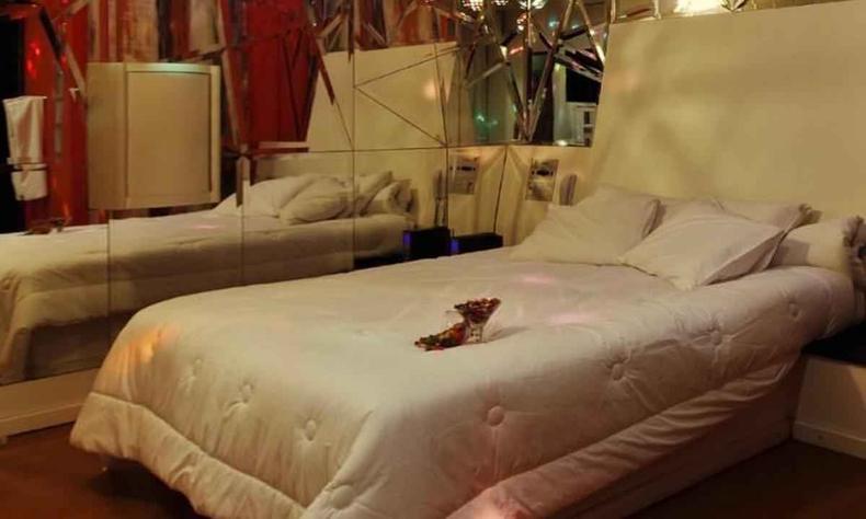 Na foto, uma das sutes do motel.  possvel ver uma cama, com enxoval branco, uma vasilha de vidro com morangos e um grande espelho do lado esquerdo