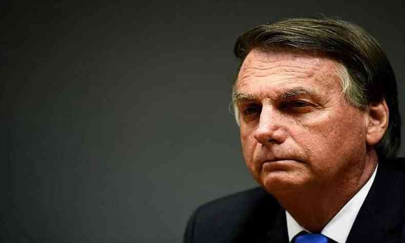 O ex-presidente Jair Bolsonaro, em foto foto na qual aparece seu rosto do lado direito da imagem. Eles usa terno preto, camisa branca e gravata azul. 