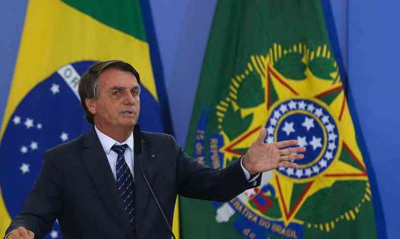 Presidente Jair Bolsonaro profere discurso em microfone. Ao fundo a bandeira do Brasil