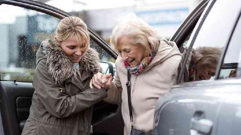 Mulher ajudando idosa a sair do carro
