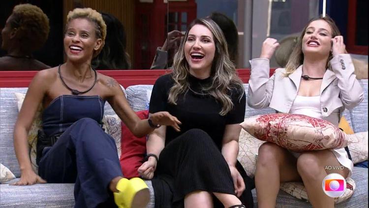 Alina, Amanda e Bruna sentadas no sof da sala do BBB e sorrindo