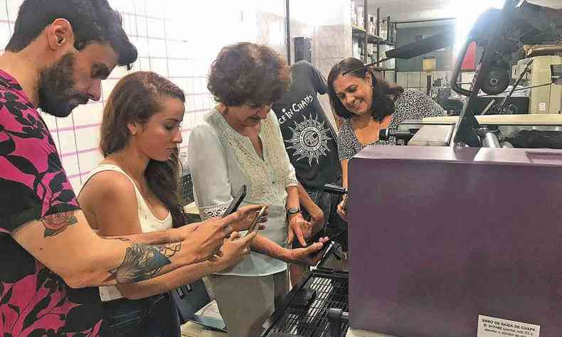Pessoas em frente a uma pequena mquina da editora Impresses de Minas, em BH, aprendem como se faz um livro.