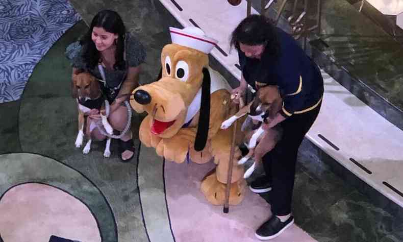 Mulheres segurando cachorros ao lado de uma pessoa fantasiada como Pluto,personagem de Walt Disney