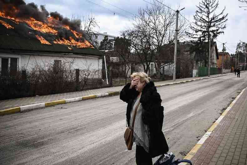Mulher lamenta em frente a uma casa em chamas bombardeada na cidade de Irpin, nos arredores de Kiev, na sexta (4).