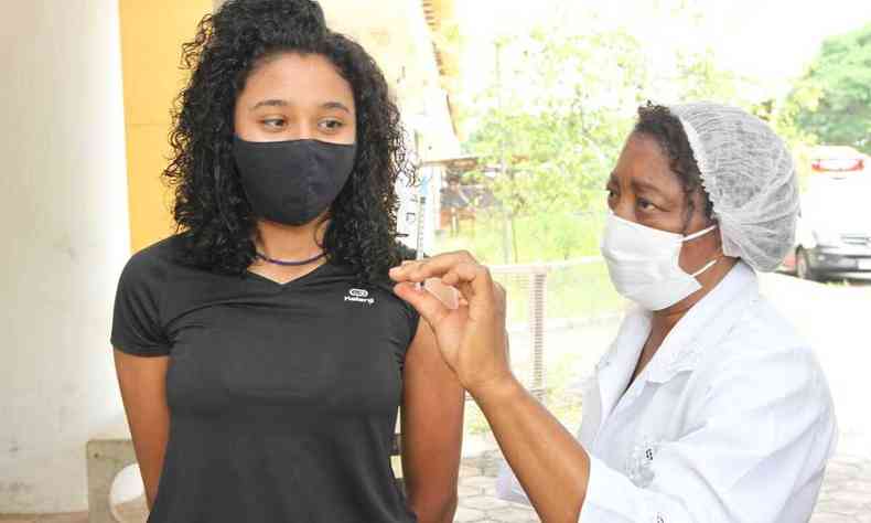 Enfermeira mostrando seringa de vacina para a adolescente 