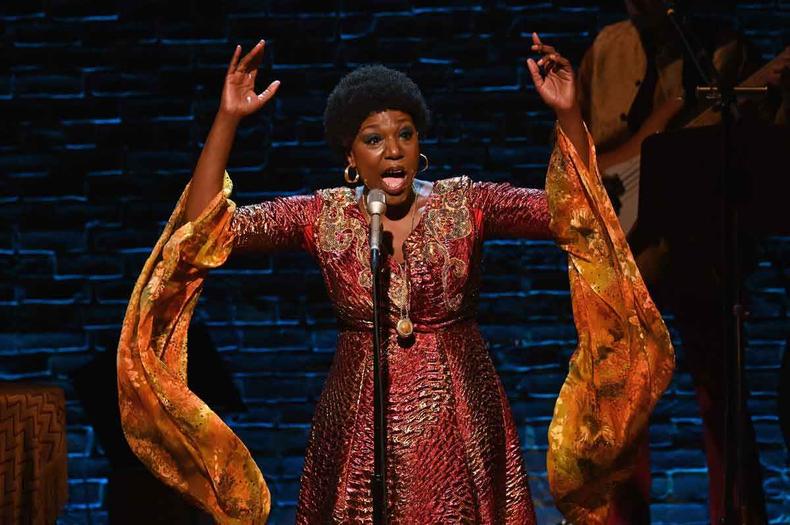 No palco, a atriz A atriz Laiona Michelle, usando vestido laranja, ergue os braos ao cantar e interpretar Nina Simone em musical em cartaz em Nova York