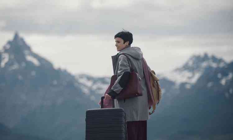 A atriz Dbora Falabella de p, segurando mala de viagem e tendo ao fundo a Cordilheira dos Andes, em cena de 'Bem-vinda, Violeta!'

