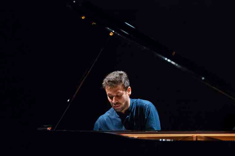 Cristian Budu sentado ao piano, de camisa azul e semblante srio, com o rosto de perfil