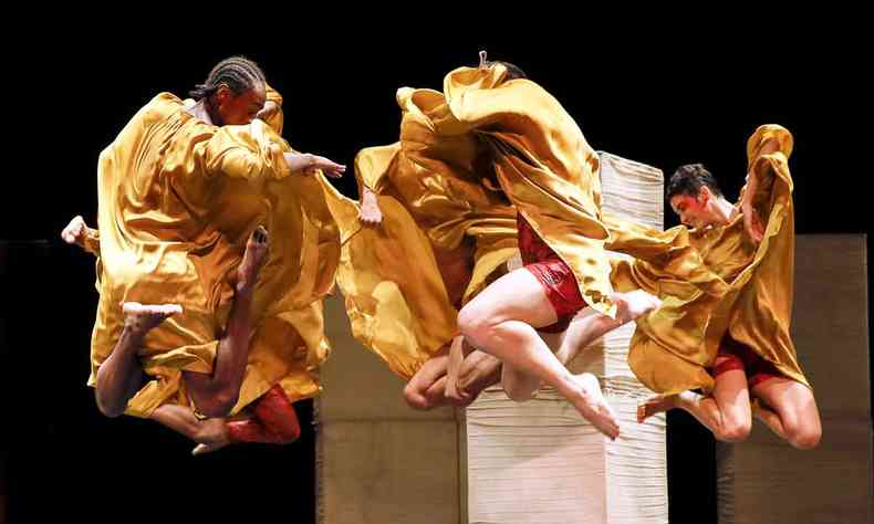 Bailarinos com figurinos laranja 'voam' sobre o palco, com as pernas encolhidas, durante Cura, espetculo da Cia. Deborah Colker