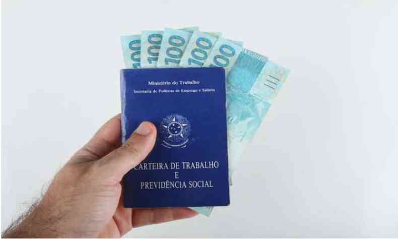 Pessoa segurando carteira de trabalho com notas de 100 reais atrs da carteira 