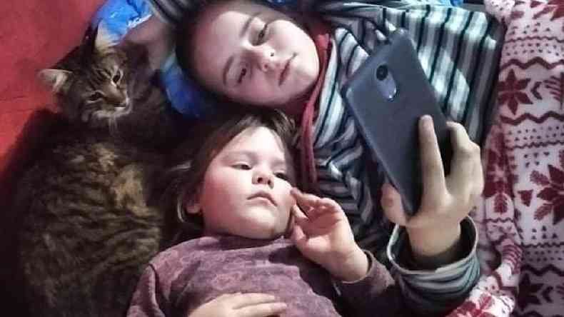 Filhas de Yuliia assistem a um vídeo no telefone de sua mãe