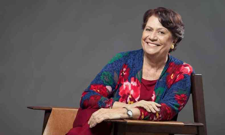 Usando roupa florida e sentada numa cadeira, a escritora Ana Maria Machado sorri para a câmera 