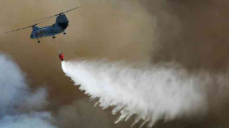 Helicptero sobrevoa um incndio florestal depositando gua