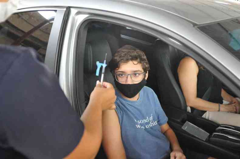 Adolescente dentro do carro olha a agulha com vacina contra COVID