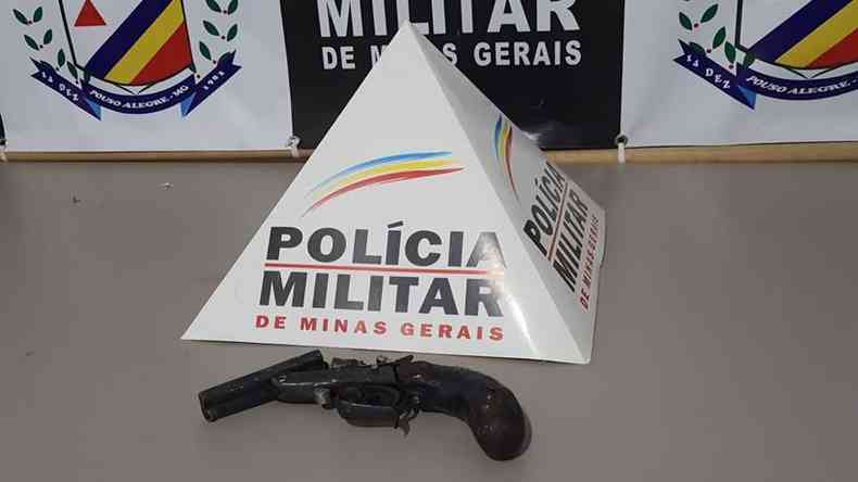 arma em cima da mesa com smbolo da PMMG ao fundo 