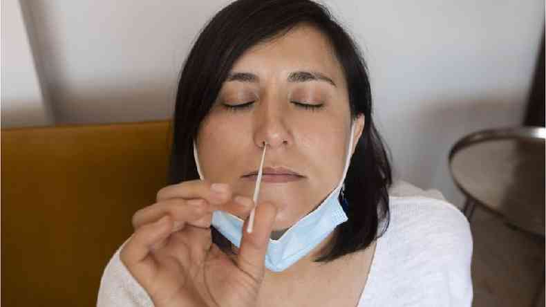 Mulher branca insere coletor de amostra em seu prprio nariz
