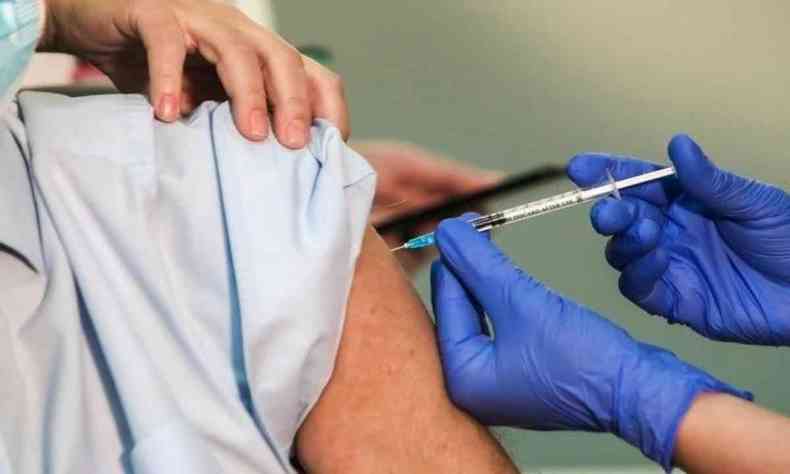 Profissional da saúde aplica vacina no braço de morador