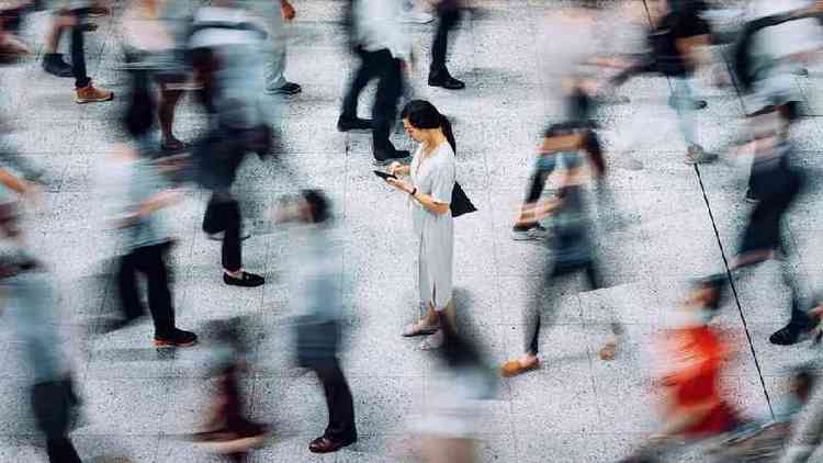 Mulher parada olhando celular enquanto outras pessoas caminham rpido ao redor