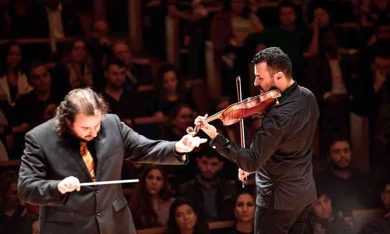 Maestro Rodrigo Toffolo com a batuta na mão ao lado de Cármelo de los Santos, que toca violino, durante concerto