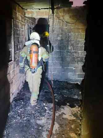 Foto vertical mostra bombeiro dentro da casa destruda pelo fogo
