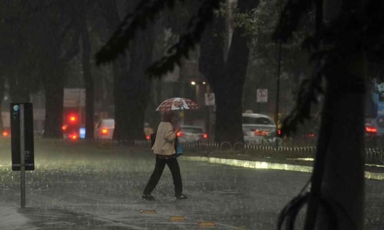 Mulher com sombrinha atravessa a rua debaixo de chuva