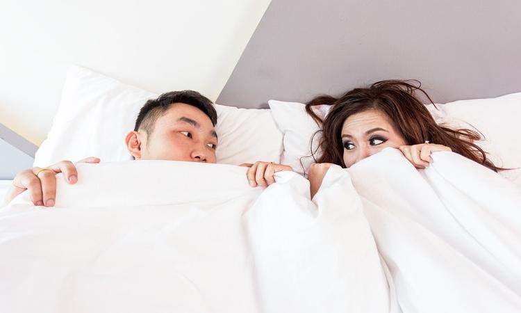 casal na cama, debaixo dos lençóis, olhando um para o outro