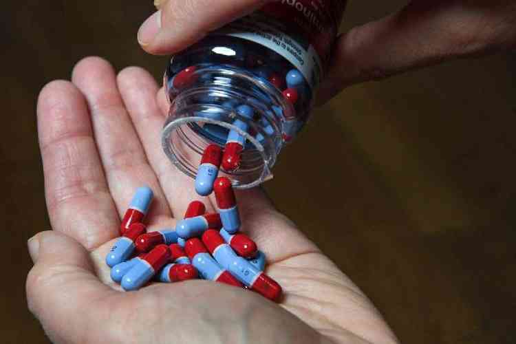 cpsulas em azul e vermelho saem de um vidro de medicamento nas mos de um homem