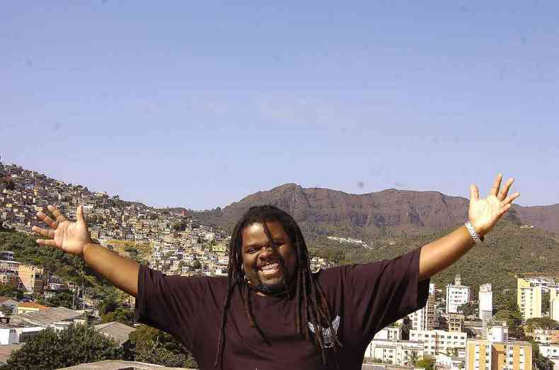 Msico Mestre Jonas posa sorrindo, de braos abertos, tendo ao fundo a favela e a Serra do Curral 