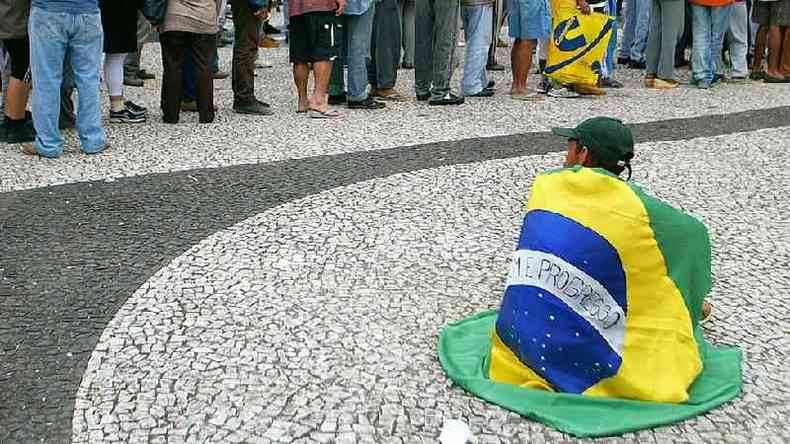 Sem teto sentado no chão enrolado na bandeira do Brasil