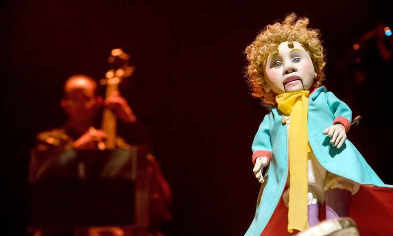Boneco est  frente do palco e ao fundo v-se violoncelista, durante concerto da Orquestra Ouro Preto 