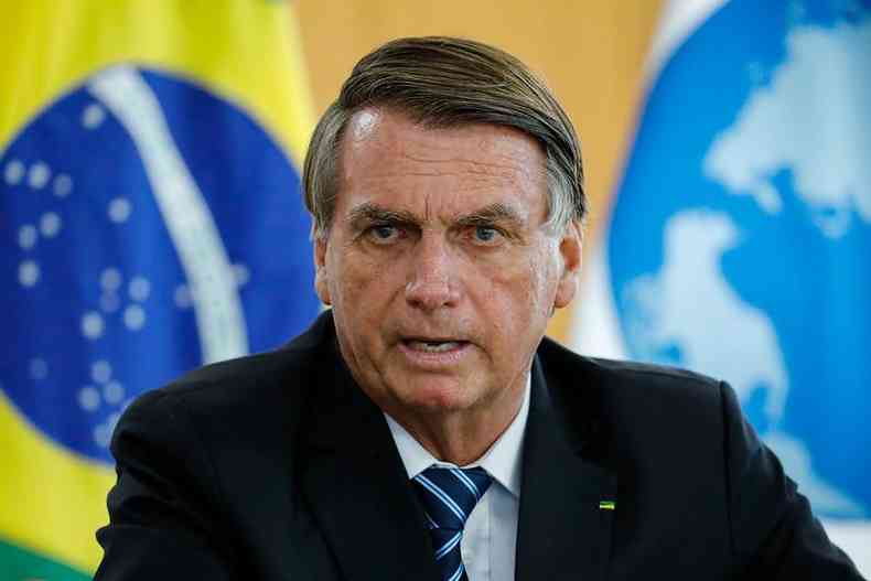 Bolsonaro fala com entrevistadores em frente a bandeira do Brasil