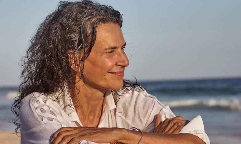 Sentada na praia, a cantora Simone sorri e olha para o lado, de braos cruzados
