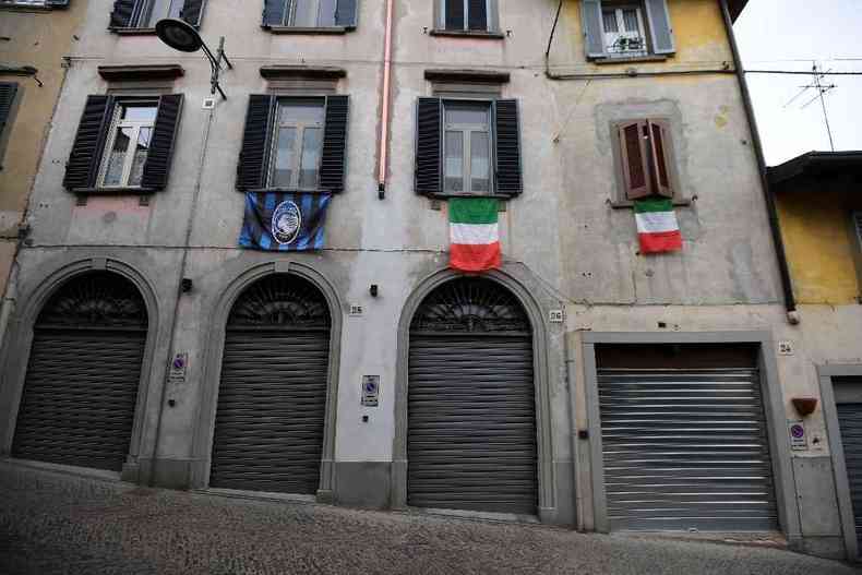Casaro fechado em rua deserta de Bergamo ostenta bandeiras da Itlia e uma do Atalanta, time de futeobl local(foto: MIGUEL MEDINA / AFP)