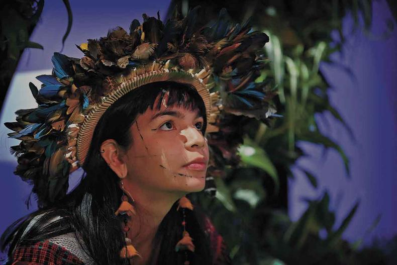 Fotografada de perfil, a jovem lder indgena brasileira Txai Suru usa cocar e olha para cima, tendo ao fundo cenrio azul e folhagens