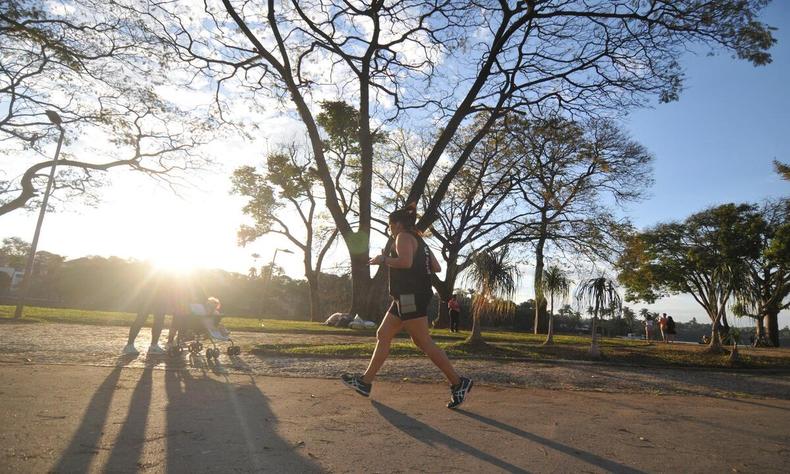 Pessoa caminhando em primeiro plano, ao fundo,  possvel ver o sol atravessando as rvores